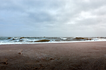 Dramatic seascape with crashing waves and cloudy sky along a deserted sandy beach.