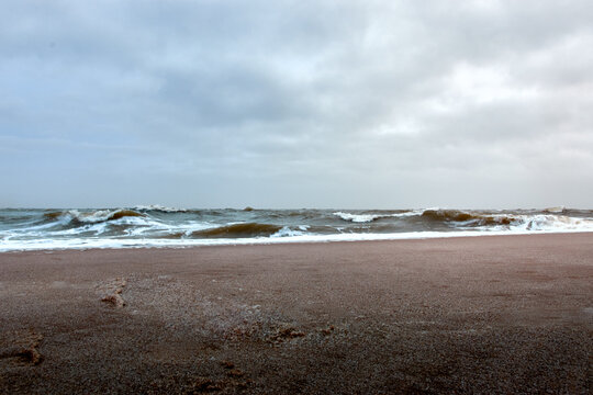 Dramatic seascape with crashing waves and cloudy sky along a deserted sandy beach. - Powered by Adobe