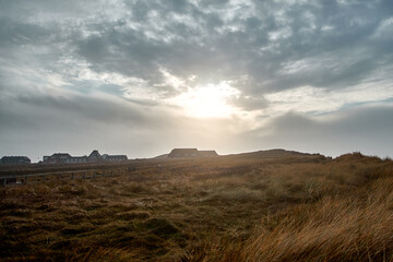 Dramatic cloudy sky over rugged coastal dunes and a historic seaside resort town.
