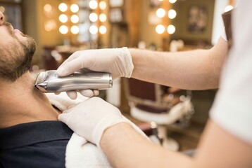 Man receiving a beard trim at a barbershop in the afternoon with a barber using an electric clipper for grooming