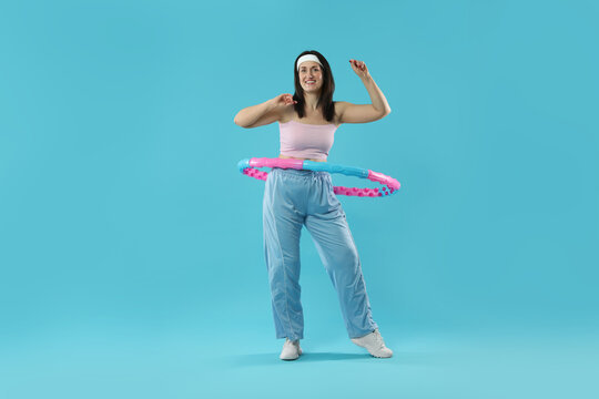 Happy woman training with hula hoop on light blue background - Powered by Adobe