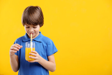 Boy with glass of fresh orange juice on yellow background. Space for text