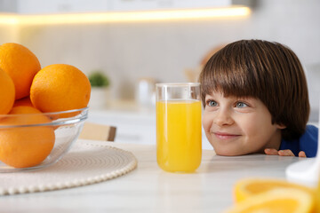 Boy with glass of fresh orange juice and fruits at table in kitchen