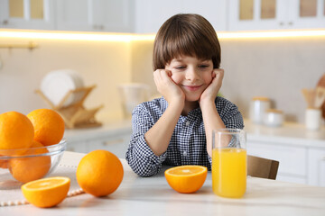 Boy with glass of fresh orange juice and fruits at table in kitchen