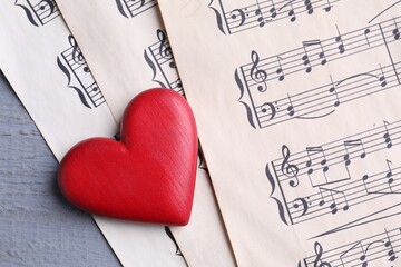 Heart figure and paper sheets with music notes on gray wooden table, top view
