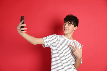 Teenage boy showing peace sign while taking selfie on red background