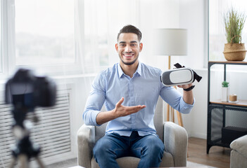 Arab male vlogger making tech product review, presenting VR headset, shooting video about cool device for technology blog at home. Eastern influencer recording brand advertising promo, using camera