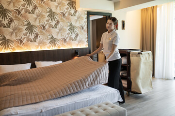 Young woman in hotel uniform doing bed in a hotel room
