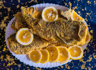 Close-up of fried fish in cornmeal next to lemon slices on a plate, homemade, traditional