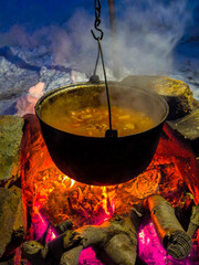 A goulash being cooked in a black cast-iron cauldron over an open fire
