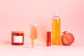 Natural cosmetic bottles with pomegranate on soft pink background. Minimal beauty still life