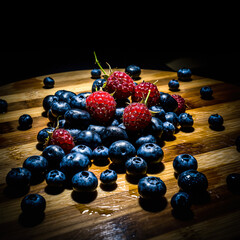 Fresh blueberries and raspberries arranged on a wooden cutting board with a dark background