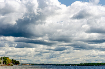 Threatening storm clouds towering over a sunlit shoreline marina at Brockville on the St. Lawerence River