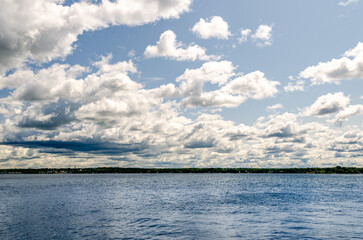 Cloud filled sky over a river with a tree-lined shore in the distance