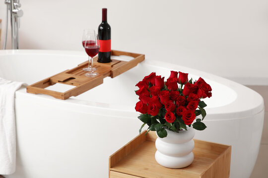 Vase with red roses on table in bathroom decorated for Valentine's Day
