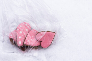 Close up of gingerbread cookies with pink icing in a transparent bag on snow