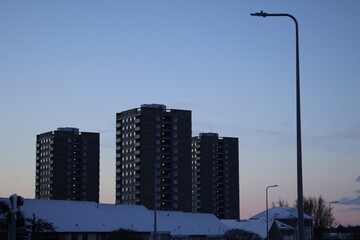 Urban winter scene with residential skyscraper buildings in the background and lamp posts.Urban winter scene with residential skyscraper buildings in the background.Bare trees,snow on the ground