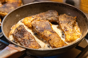 Golden brown carp fillets frying in a pan with sizzling oil, a traditional Polish Christmas Eve dish being prepared in a home kitchen.