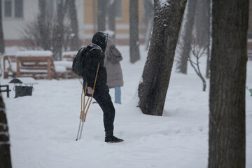 A lonely one-legged man on crutches walks along a snowy street