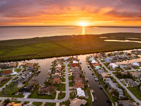 Sunset aerial view of Punta Gorda wealthy neighborhood. Expensive residential homes along canals reflect warm evening sky.