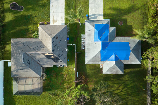Top view of leaking house roof covered with protective tarp sheets against rain water leaks until replacement of asphalt shingles. Damage of building rooftop as aftermath of hurricane Ian in Florida