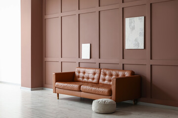 Sofa with pouf and paintings on brown wall in room