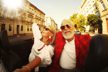 Fototapeta premium Stylish elderly couple enjoying ride in convertible car on sunny day, wide angle lens