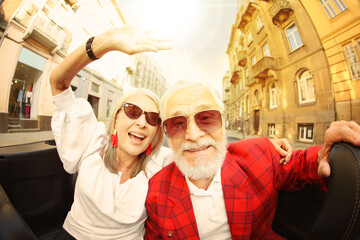 Stylish elderly couple enjoying ride in convertible car, wide angle lens