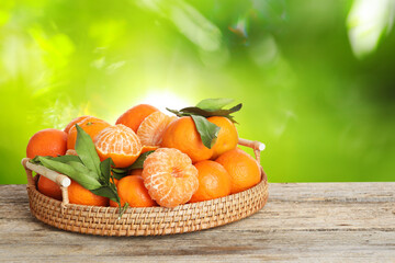 Fresh juicy tangerines in wicker tray on wooden table outdoors