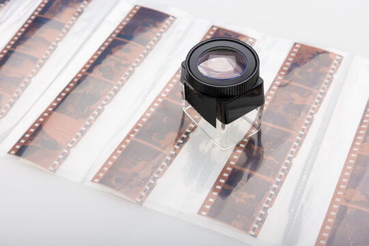 Colour negative film strips with viewing loupe on light table.