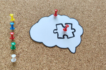 Missing puzzle piece completing a brain symbol on a cork board. Mental health and problems with memory.