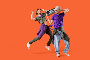 Young couple with boombox dancing on orange background