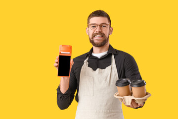 Male barista with payment terminal and coffee cups on yellow background