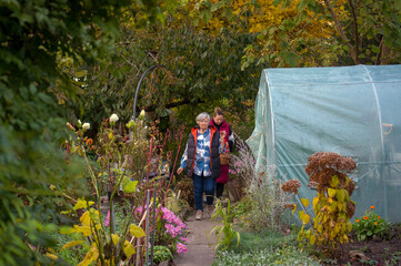 Mama z córką idące po ścieżce ogrodowej w otoczeniu drzew i kwiatów. © Monika