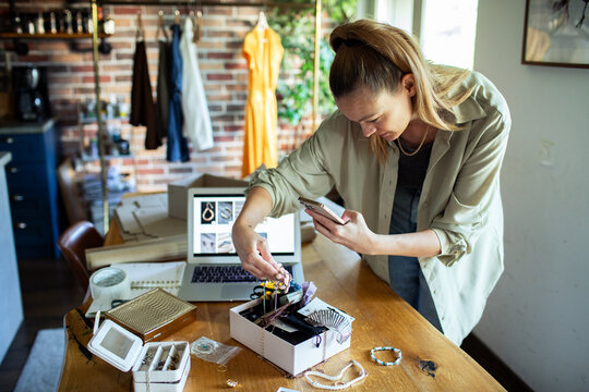 Young adult woman focused photographing handmade jewelry at home
