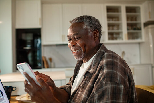 Happy senior man using smartphone in home kitchen