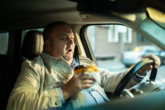 Adult man yawning with coffee and pastry while driving in car
