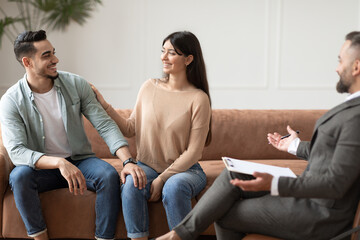 Obraz premium Couples Therapy Concept. Happy husband and wife reconciling at session in therapists office during appointment, looking at each other, smiling woman touching man's shoulder, sitting on couch sofa