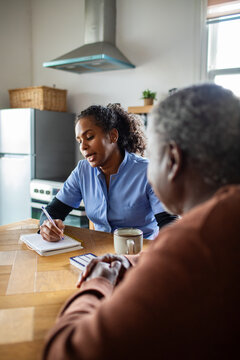 Young adult caregiver attentively explaining care plan to senior in home kitchen
