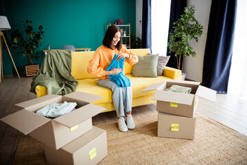 Woman packing seasonal clothes in a bright living room with labeled boxes ready for a spring and...