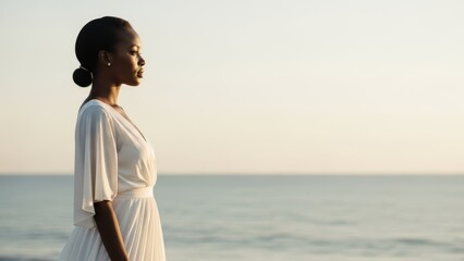 Elegant African American woman in white dress contemplating the ocean horizon during a serene sunrise