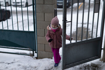 girl opening metal gate stepping outside into snowy path, determined small hand on latch,...