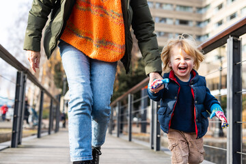 Happy toddler laughing walking outdoors holding parent hand