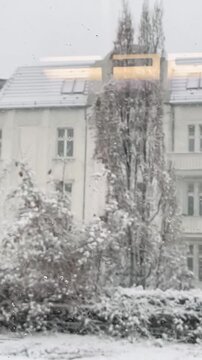 snowy building seen through window, historic pale faade dusted with snow, poplar and bare trees, motion blur from passing train, interior light Vertical shot taken on mobile device.