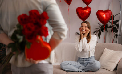 Man hiding red roses and heart shaped gift box behind back to surprise girlfriend for Valentine's Day
