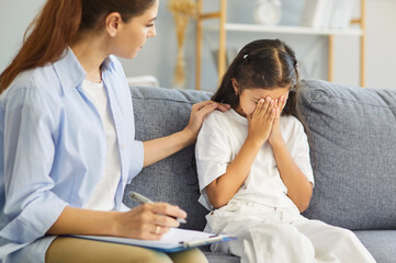 Obraz premium Psychologist supports upset child girl during therapy session. Counselor offers comfort, resting a hand on shoulder as tears reflect anxiety. Psychotherapy and kids mental health concept.