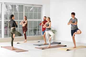 Obraz premium Group of sporty people with instructor practicing yoga in gym