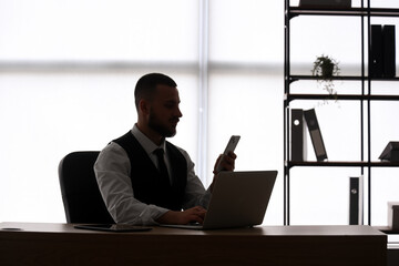 Silhouette of young businessman with laptop and mobile phone near window. Data science concept