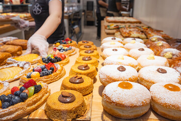 Fresh pastries and fruit tarts displayed at a bakery counter while staff prepare baked goods inside a busy bakery