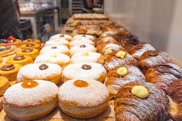 Fresh pastries and fruit tarts displayed at a bakery counter while staff prepare baked goods inside a busy bakery